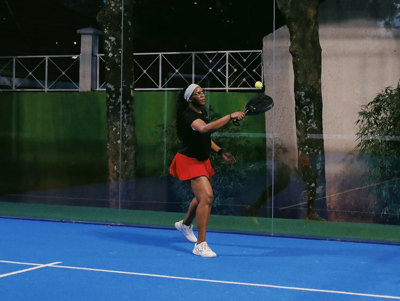 Tonia competing on a blue padel court in a red skirt.